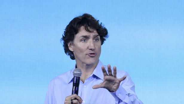 Justin Trudeau mit Mikrofon gestikuliert vor einem hellblauen Hintergrund.