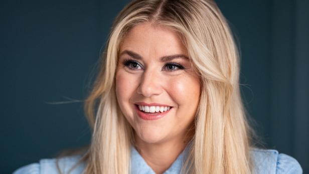 Beatrice Egli lächelt freundlich vor einem dunklen Hintergrund.