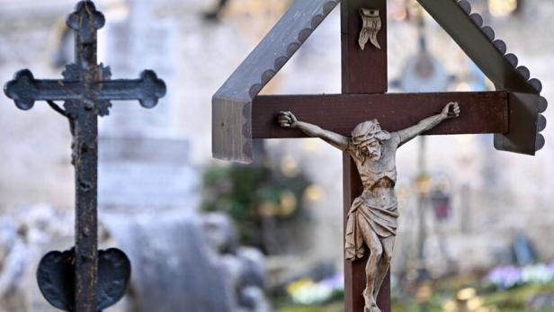 Holzkreuz mit Jesusfigur im Vordergrund, weitere Kreuze und unscharfe Gräber im Hintergrund.