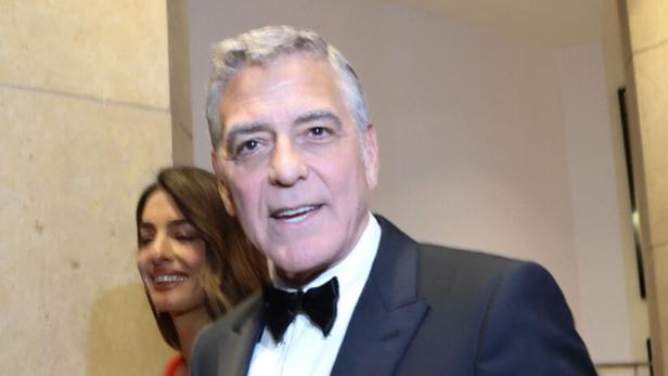 George Clooney im Smoking mit Amal Clooney in rotem Kleid.