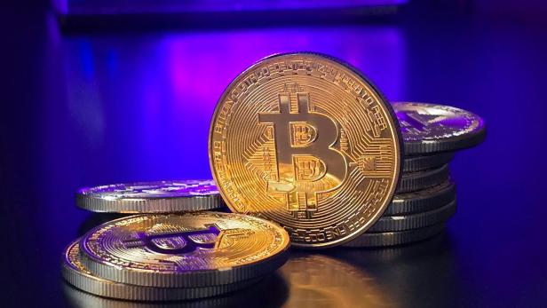 Bitcoin und Münzen liegen auf einem Tisch, beleuchtet von einem lila Licht.