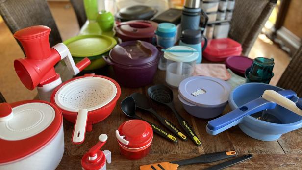 Auf einem Holztisch stehen viele Küchenutensilien in buntem Plastik