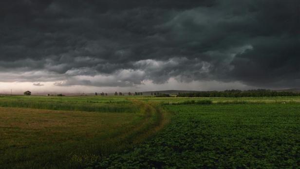 Dunkle Gewitterwolken ziehen über eine grüne Landschaft mit Feldern und Wiesen.