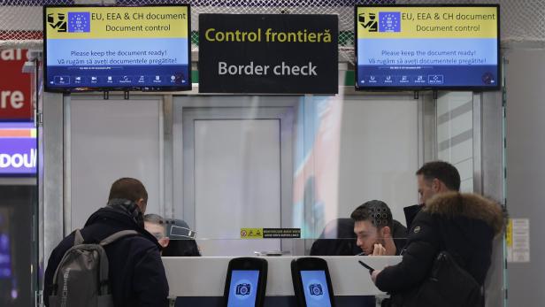 Reisende stehen an einem Schalter zur Grenzkontrolle mit Bildschirmen, die Dokumentenkontrollen anzeigen.