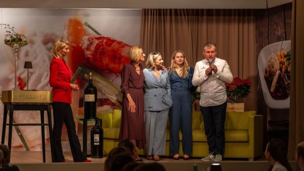 Fünf Personen stehen auf einer Bühne vor einem großen Essensmotiv, während eine Person ins Mikrofon spricht.