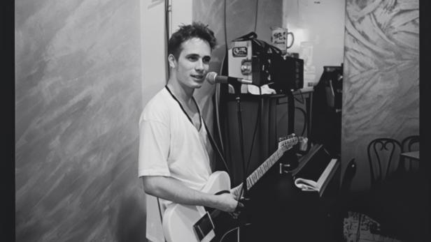 Schwarzweißes Foto des jungen Musikers Jeff Buckley in weißem T-Shirt an seiner Gitarre im Studio
