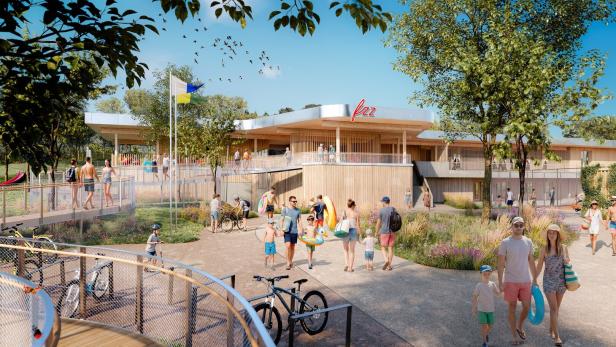 Viele Menschen in Sommerkleidung gehen mit Schwimmutensilien zu einem modernen Freizeitbad mit Holzfassade und grüner Umgebung.