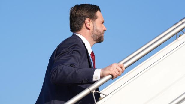Vance steigt eine Flugzeugtreppe vor blauem Himmel hinauf.