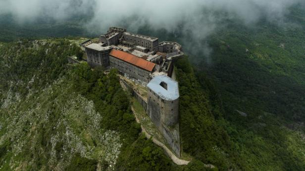 Eine Festung thront auf einem bewaldeten Hügel, teilweise von Nebel umhüllt.