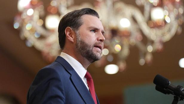 JD Vance spricht am Rednerpult mit Mikrofon und trägt einen dunklen Anzug mit roter Krawatte.
