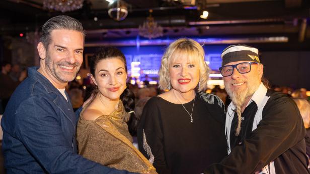 Vier lächelnde Personen legen ihre Hände übereinander in einem festlichen Rahmen.