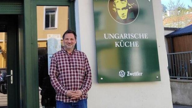 Ein Mann steht vor dem Restaurant "Ungarische Küche" mit einem Schild von Zwettler.