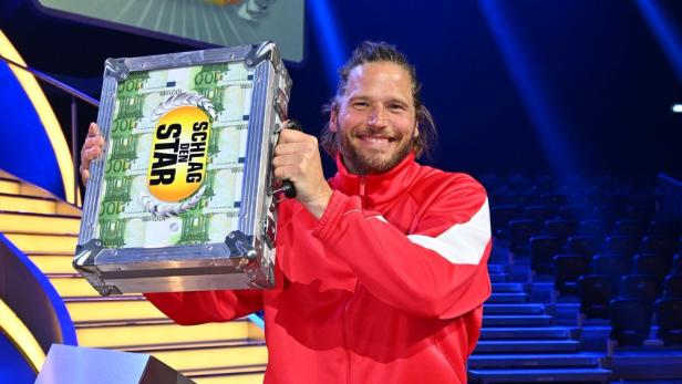 Sebastian Ströbel hält den Geldkoffer lächeln hoch