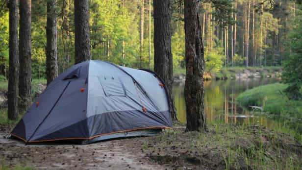 Graues Zelt steht in einem Waldgebiet nahe eines Gewässers