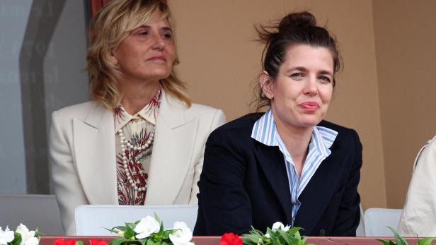 Charlotte Casiraghi sitzt neben einer blonden Frau in einem hellen Blazer vor einem mit Blumen geschmückten Balkongeländer.