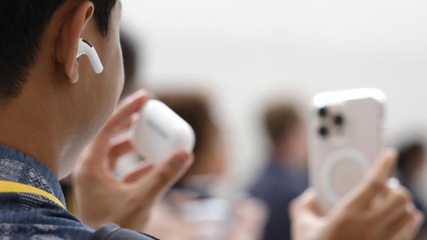 Eine Person hält AirPods-Kopfhörer und ein iPhone in der Hand
