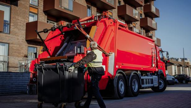 Roter Müll-LKW, frau fährt dahinter mit Mülltonne