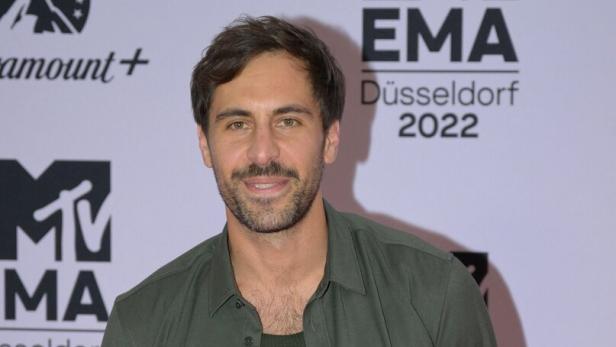 Max Giesinger mit Bart und offenem Hemd posiert vor einem MTV EMA Düsseldorf Hintergrund.