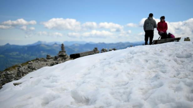 Zwei Personen stehen auf einer verschneiten Bergkuppe mit Steinmännchen und Blick auf eine Berglandschaft.