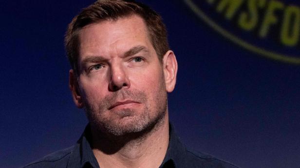 Ein Mann mit kurzem Bart und ernster Miene vor dunkelblauem Hintergrund mit unscharfer gelber Schrift.