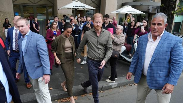 Harry und Meghan gehen Händchen haltend durch eine Menschenmenge.
