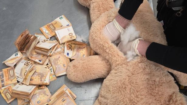 Ein Teddybär wird geöffnet, zahlreiche 50-Euro-Scheine liegen auf dem Tisch daneben.