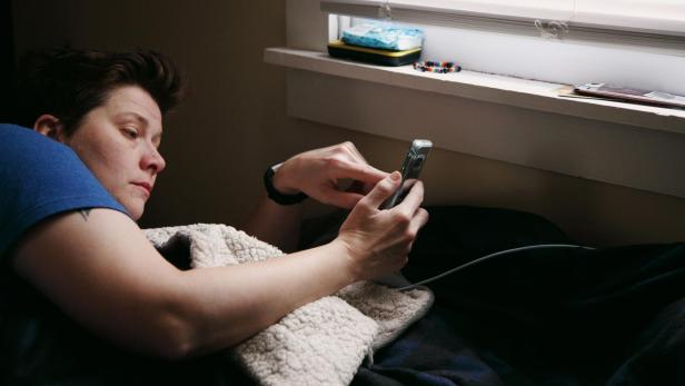 Frau liegt krank im Bett und nimmt Video auf.