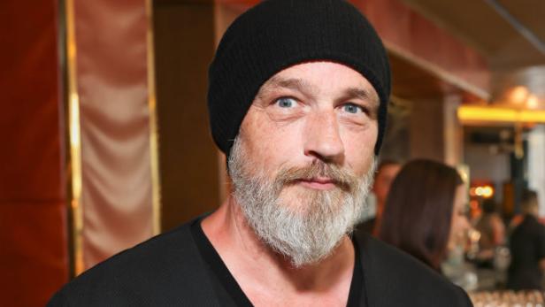 Torsten Sträter mit schwarzer Mütze und Glas Wein in der Hand bei einer Veranstaltung.