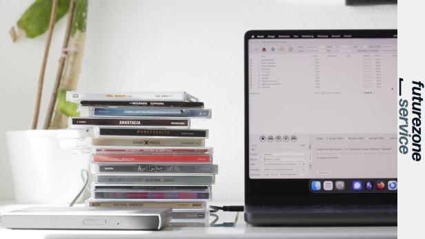 Ein Stapel CDs neben einem Laptop mit geöffneter Ripping-Software und externem Laufwerk.
