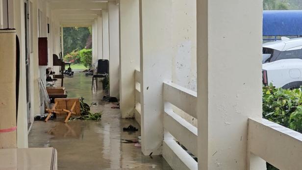Ein überdachter Gang mit umgestürzten Stühlen, verstreuten Gegenständen und nassem Boden nach starkem Regen.