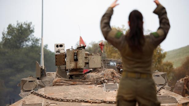 Eine Person in Militäruniform steht mit erhobenen Armen vor einem Panzer, im Hintergrund Bäume und Hügel.