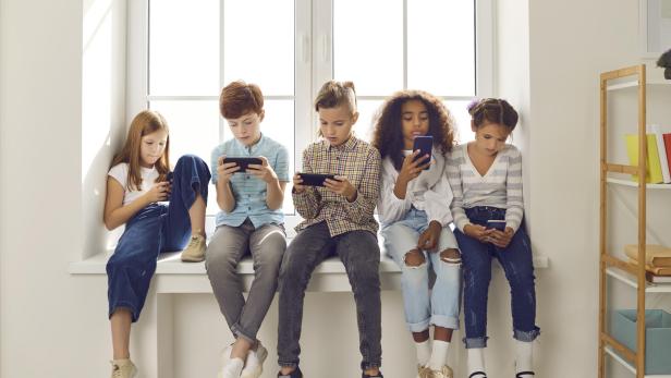 Fünf Kinder sitzen nebeneinander auf einer Fensterbank und schauen auf ihre Smartphones