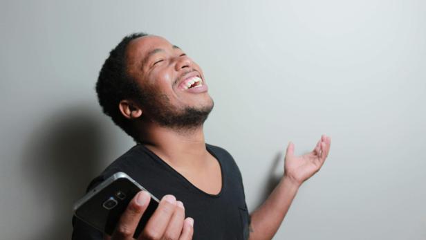 Mann lacht erleichtert und hält ein Smartphone in der Hand.