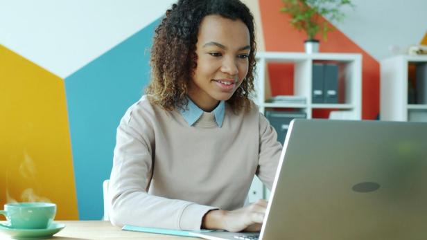 Frau arbeitet an einem Laptop in modern gestaltetem Büro mit bunter Wand und Pflanzen.