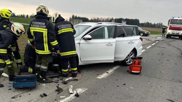 Feuerwehr-Helfer vor einem weißen Unfallwrack