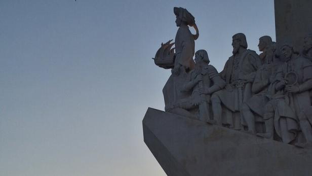 Das Denkmal der Entdeckungen in Lissabon zeigt Skulpturen vor einem Sonnenuntergang über dem Tejo.