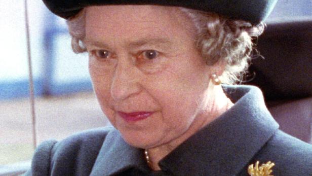 Queen Elizabeth II. mit elegantem dunklen Mantel, großem Hut und goldener Brosche, schaut konzentriert nach vorne.