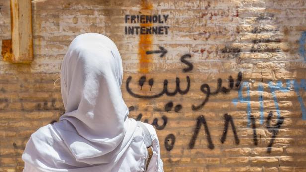 Veiled woman watching inscription on wall indicating uncensored Internet spot
