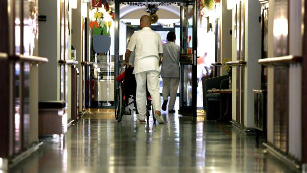 Altenpfleger schiebt Rollstuhl in Pflegeheim