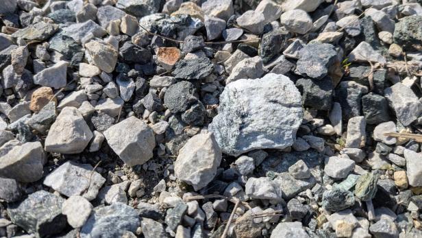 Viele kleine, unterschiedlich geformte Steine in verschiedenen Grautönen liegen dicht nebeneinander auf dem Boden.