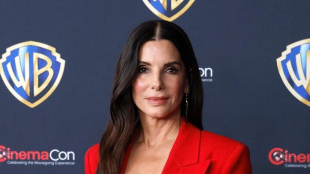 Sandra Bullock trägt einen roten Hosenanzug vor einem Warner Bros. Hintergrund.