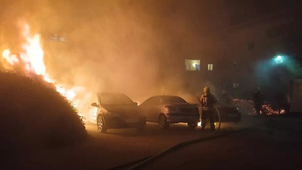 Starke Flammen und dichter Rauch umgeben mehrere Autos, während Feuerwehrleute versuchen, das Feuer zu löschen.