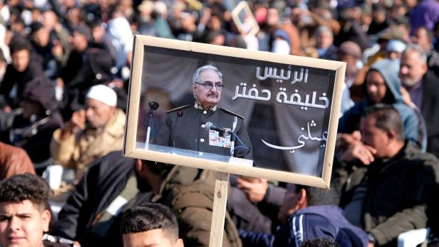 Menschenmenge im Freien, jemand hält ein Schild mit dem Porträt eines Mannes in Uniform und arabischer Schrift hoch.