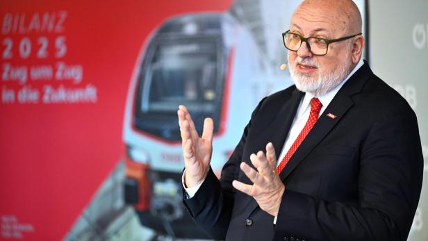 Ein Mann mit Brille und Anzug präsentiert vor einem ÖBB-Zug und der Aufschrift "Bilanz 2025".