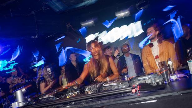 Naomi Campbell legt als DJane in einem vollen Club vor tanzendem Publikum auf.