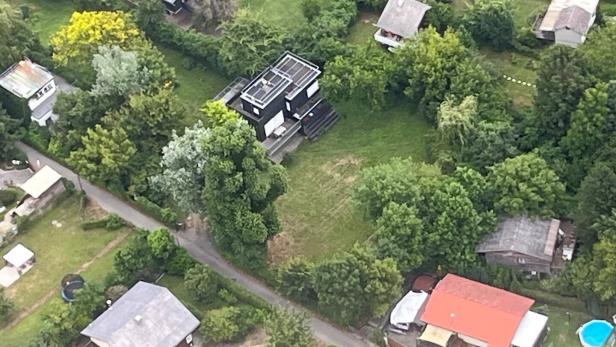 Luftaufnahme von Wohnhäusern mit Gärten und Bäumen in einer grünen Landschaft.