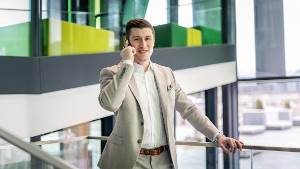 Junger Mann im Anzug telefoniert in einem modernen, lichtdurchfluteten Bürogebäude.
