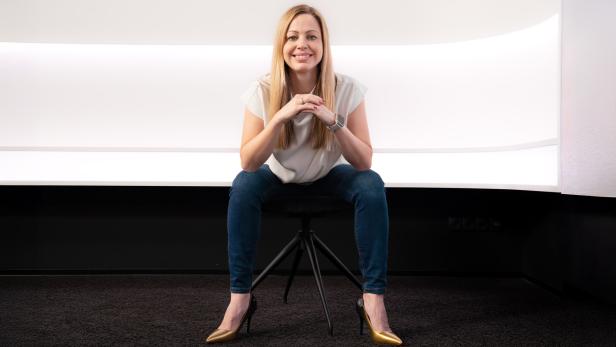 Eine Frau sitzt auf einem Stuhl vor einer weißen Wand.