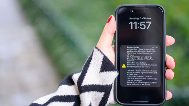 Eine Hand hält ein Smartphone, das eine Warnmeldung des Bundesministeriums für Inneres anzeigt.