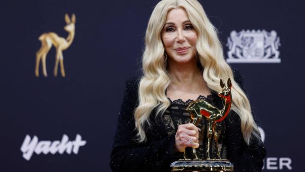 Cher hält eine goldene Bambi-Trophäe vor einem dunklen Hintergrund.